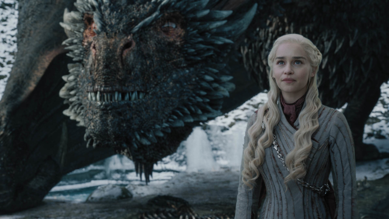 Queen Daenerys Targareon standing proudly in her white dress, while Drogon the main dragon is guarding her from behind.